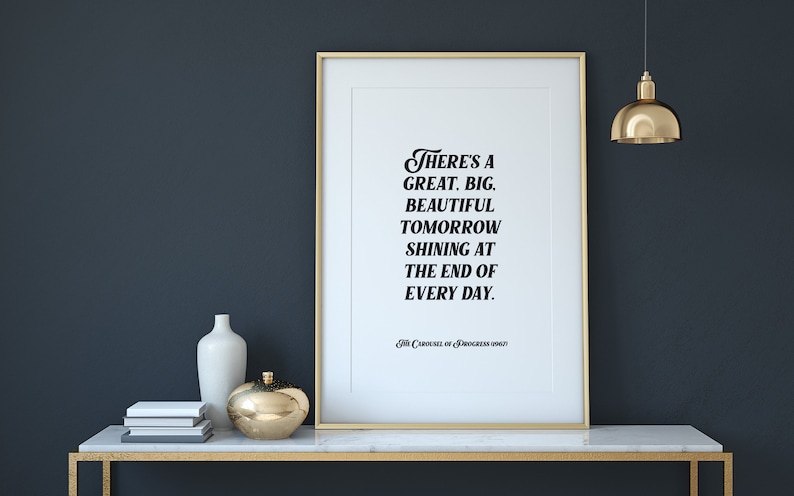 May include: A framed print with a gold frame and a white background. The print features a black and white quote that reads "There's a great, big, beautiful tomorrow shining at the end of every day." The quote is attributed to "The Carousel of Progress" at the bottom of the print.