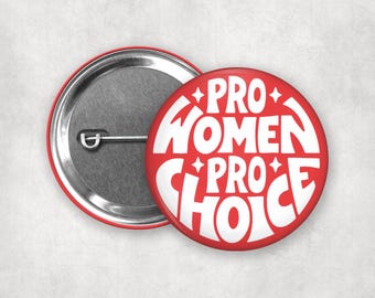 Può includere: Due bottoni rotondi rossi. Un bottone mostra il retro con una spilla d'argento. L'altro bottone mostra il fronte con le parole "PRO WOMEN PRO CHOICE" in bianco, con accenti a stella.