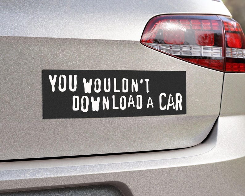 Peut inclure: Un aimant de voiture rectangulaire noir avec le texte blanc "YOU WOULDN'T DOWNLOAD A CAR" est fix&eacute; &agrave; l'arri&egrave;re d'une voiture argent&eacute;e. L'aimant est positionn&eacute; sous le feu arri&egrave;re.