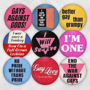 May include: A collection of nine colorful round buttons with various text designs. The buttons feature phrases like "Gays Against Gods!", "I'm One", and "Gay Love". The buttons are in shades of pink, blue, yellow, red, and black.