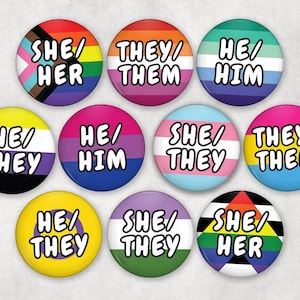 May include: A collection of ten round pronoun pins. Each pin features a different design with the pronouns "She/Her", "They/Them", or "He/Him", and the colors of various pride flags.
