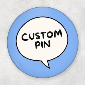 Puede incluir: Un pin redondo azul claro con las palabras "CUSTOM PIN" en negro, dentro de una burbuja de diálogo blanca. El pin tiene un acabado brillante y un borde negro alrededor de la burbuja.