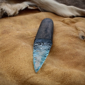 May include: A blue glass knife with a wooden handle. The knife is lying on a brown leather surface.