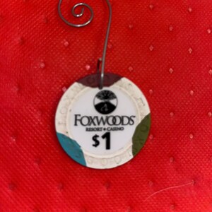 May include: A white round casino chip with a brown, green, and blue border. The chip has the text "Foxwoods Resort Casino" and "$1" printed on it.