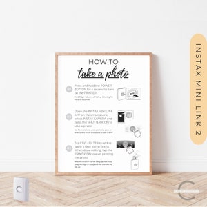 Puede incluir: Un póster blanco con texto negro e ilustraciones que muestran cómo tomar una foto usando la impresora Instax Mini Link 2. El póster tiene tres pasos: 1. Encienda la impresora, 2. Abra la aplicación Instax Mini Link y seleccione Instax Camera, 3. Toque Editar/Filtro para editar o aplicar un filtro a la foto. Cuando haya terminado de editar, toque el icono Imprimir para comenzar a imprimir la foto.
