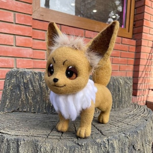 May include: A brown and white felt fox plush toy with a white collar and brown eyes. The toy is sitting on a tree stump.