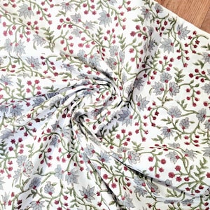 Puede incluir: Tela blanca con un estampado floral. El diseño presenta flores grises, pequeños capullos rojos y tallos y hojas verdes. La tela está doblada, creando sombras y textura.