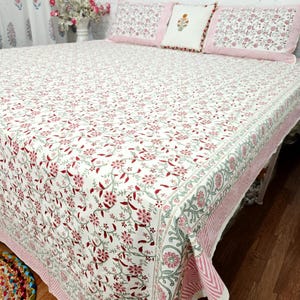 May include: A white bedspread featuring a repeating floral pattern in shades of red and green, finished with a pink striped border. The set includes two matching rectangular pillow shams and one square decorative pillow with a central floral motif.
