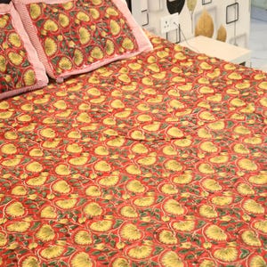Puede incluir: Una colcha roja y dos fundas de almohada a juego con un diseño floral. El patrón presenta flores amarillas y hojas verdes sobre un fondo rojo. Las fundas de almohada tienen un borde a rayas.