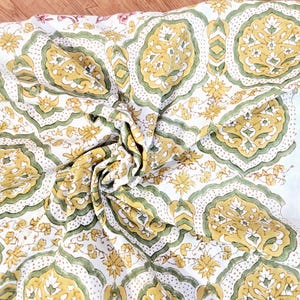 Peut inclure: Tissu blanc avec un motif répété de médaillons floraux jaunes et verts. Le motif comprend de petites fleurs jaunes et des accents verts sur un fond blanc. Le tissu est plié, révélant la texture et les détails du motif.