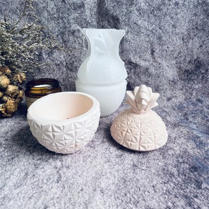 May include: A set of three white and pink ceramic pineapple-shaped containers. The containers have a geometric pattern and are ideal for storing small items.