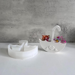 May include: White silicone mould for making a small umbrella-shaped planter. The mould is shown with dried flowers inside. The mould is designed to create a planter with three hearts on the front.