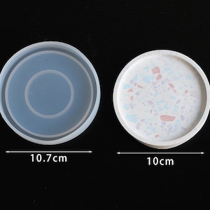 May include: Two round silicone moulds for resin crafts. The mould on the left is 10.7 cm in diameter and has a raised ring in the centre. The mould on the right is 10 cm in diameter and has a white speckled finish.