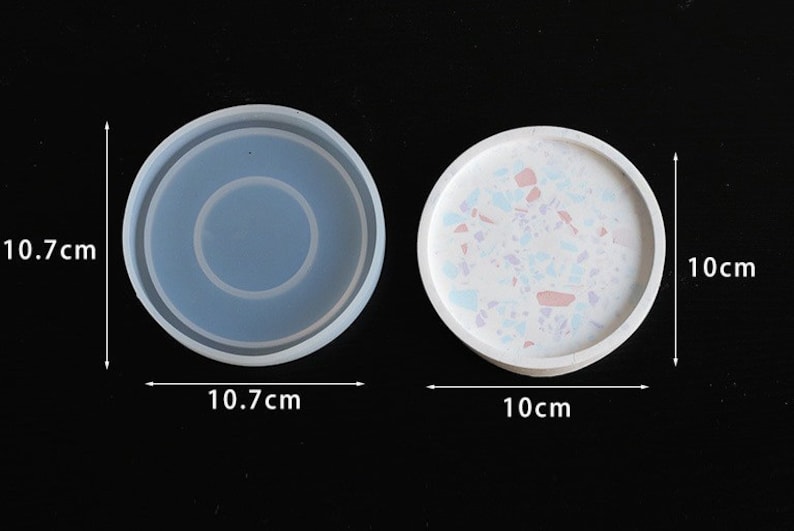 May include: Two round silicone moulds for resin crafts. The mould on the left is 10.7 cm in diameter and has a raised ring in the centre. The mould on the right is 10 cm in diameter and has a white speckled finish.