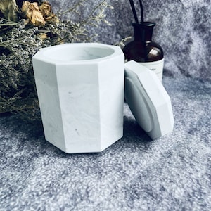 May include: White octagonal concrete container with a matching lid. The container has a textured surface and is ideal for storing small items.