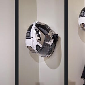 Può includere: Ganci per casco in plastica bianca montati su una parete bianca. Il gancio ha un braccio curvo per tenere un casco.