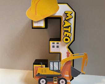 Può includere: Un topper per torta a forma di numero tre a tema costruzione, giallo e nero, con un casco giallo, un piccolo escavatore e il nome Mateo.