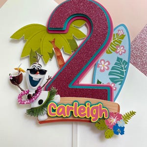 May include: A colorful birthday cake topper featuring the number 2 in glittery magenta, outlined in teal and pink. Includes a cartoon Olaf character, a surfboard, palm tree, and the name "Carleigh".