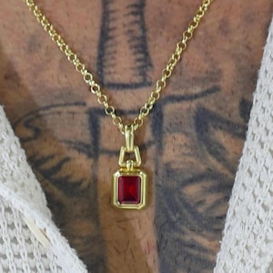 May include: A gold chain necklace with a square pendant featuring a red gemstone.