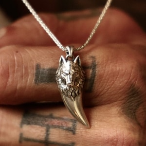 May include: A silver pendant necklace with a wolf head and claw design. The pendant hangs from a fine silver chain. The necklace is a striking piece of jewellery, suitable for everyday wear or special occasions.
