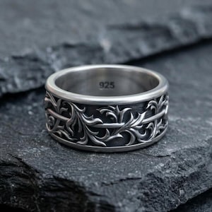 May include: A silver-toned metal ring featuring an intricate, raised vine and leaf pattern wrapping around the exterior band. The interior of the ring is smooth and clearly stamped with the text 925, indicating the metal composition.