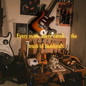 K&ouml;nnte beinhalten: Werkstatt mit Werkzeugen und Gitarren. Der Text lautet: &bdquo;Jede Markierung, jedes Detail... die Wahrheit des Handwerks.&ldquo; Eine Fender-Gitarre befindet sich links, und eine Sunburst-E-Gitarre h&auml;ngt &uuml;ber der Werkbank.