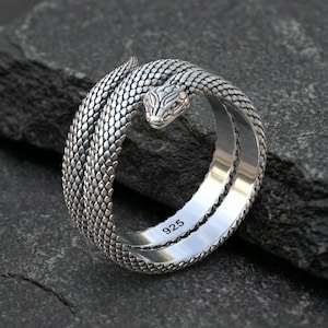 May include: A silver ring in the shape of a snake coiled around itself. The snake's head is raised, and the ring is detailed with scales. The inside of the ring is stamped with "925".