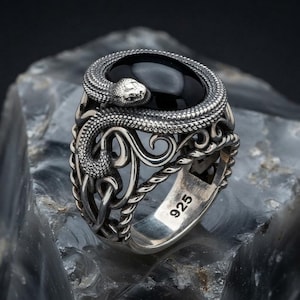 Puede incluir: Un anillo de plata de ley con una serpiente enroscada alrededor de una piedra de ónice negra lisa de forma ovalada. La banda muestra intrincados patrones de metal calado y está claramente marcada con el número 925 en la superficie interior.