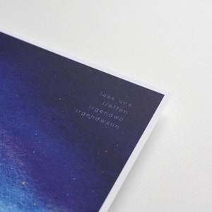 Peut inclure: Une impression aquarelle bleue et violette avec un fond de ciel &eacute;toil&eacute;. Le texte "lass uns treffen irgendwo irgendwann" est imprim&eacute; en blanc dans le coin inf&eacute;rieur droit de l'impression.