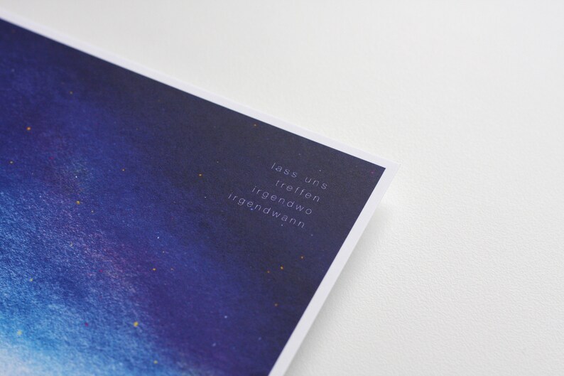 Peut inclure: Une impression aquarelle bleue et violette avec un fond de ciel &eacute;toil&eacute;. Le texte "lass uns treffen irgendwo irgendwann" est imprim&eacute; en blanc dans le coin inf&eacute;rieur droit de l'impression.