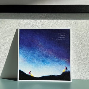Peut inclure: Une illustration &agrave; l'aquarelle de deux personnes &agrave; v&eacute;lo qui montent des collines sur fond de ciel nocturne &eacute;toil&eacute;. Le texte "lass uns treffen irgendwo irgendwann" est &eacute;crit dans le coin sup&eacute;rieur droit de l'image.