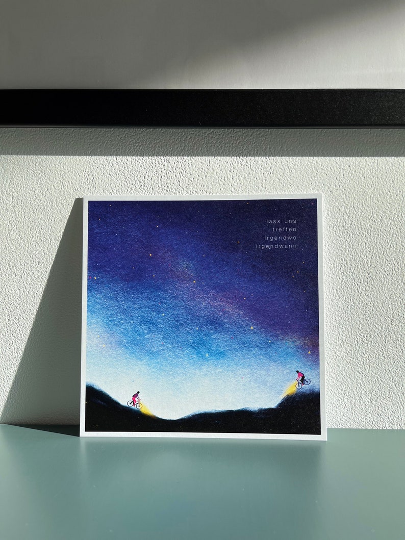Peut inclure: Une illustration &agrave; l'aquarelle de deux personnes &agrave; v&eacute;lo qui montent des collines sur fond de ciel nocturne &eacute;toil&eacute;. Le texte "lass uns treffen irgendwo irgendwann" est &eacute;crit dans le coin sup&eacute;rieur droit de l'image.