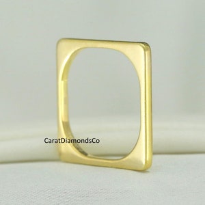 Puede incluir: Un anillo cuadrado simple de oro con un acabado liso y pulido. El anillo está hecho de oro macizo y tiene un diseño moderno y minimalista.