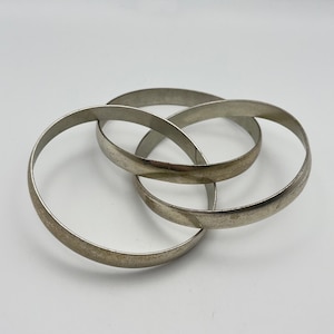 May include: Three silver metal bangles interlocked together. The bangles are smooth and shiny.