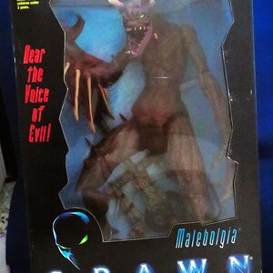 May include: A boxed Malebolgia action figure from the film Spawn. The figure is a detailed, brown demon with sharp claws and glowing green eyes. The box features the Spawn logo and the text "Hear the Voice of Evil!"