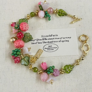 Peut inclure: Un bracelet en or avec un charme de fleur rose, de feuilles vertes et de fraises rouges. Le bracelet porte une étiquette qui indique "French Paris" et "Imef You The dead tree of spring".