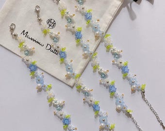 May include: Four delicate beaded bracelets with blue and white flowers and pearl accents. The bracelets have silver clasps and chains. The bracelets are displayed on a white fabric bag with the text "Massimo Dutti" printed on it.