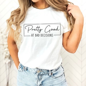 Op de afbeelding: Wit T-shirt met de tekst "Pretty Good at Bad Decisions" in zwart gedrukt.