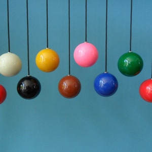 May include: Nine colourful spherical pendant lights suspended from black cords against a teal backdrop. The lights are in a range of colours, including red, yellow, and blue. The glossy spheres reflect light, creating a modern aesthetic.