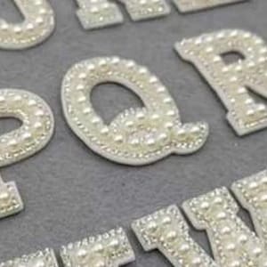 May include: White pearl alphabet letters for crafting and decorating. Each letter is made of white pearls sewn onto a white fabric backing.