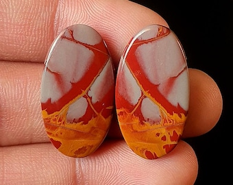 May include: Two oval-shaped gemstones with a polished finish. The stones feature a striking pattern of red veins against a creamy white background, with a band of orange and yellow at the base. The text "M-1928" is in the upper right corner.