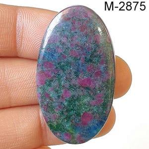 May include: Oval-shaped gemstone with a mix of colors. The stone features a base of green and blue hues, speckled with vibrant red spots. The text "M-2875" is visible in the upper right corner.