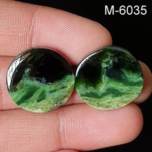 May include: Two circular, polished gemstones displaying a blend of dark green and black hues. The stones have a glossy finish and a marbled effect, with the text "M-6035" visible in the upper right corner.