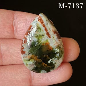 May include: A teardrop-shaped gemstone with a polished surface. The stone features a mix of colors, including green, red, and white, with a marbled appearance. The text "M-7137" is visible in the upper right corner.