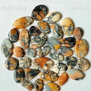 May include: A collection of 25 oval-shaped, polished, natural gemstone cabochons. The stones are a mix of brown, grey, and white with intricate patterns. The stones are approximately 2.5 cm in length.