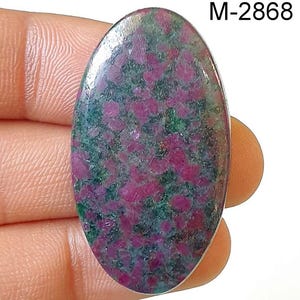 Może przedstawiać: Owalny kamień szlachetny w szlifie kaboszonowym z zielono-różowym wzorem w kropki. Kamień ma około 6,5 cm długości i 4 cm szerokości. M-2868