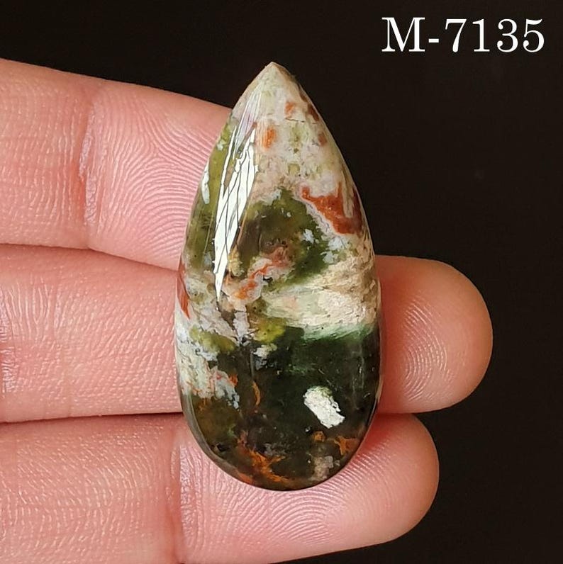 May include: A teardrop-shaped gemstone with a polished surface. The stone features a mix of colors, including green, white, orange, and brown, with a marbled appearance. The text "M-7135" is visible in the upper right corner.