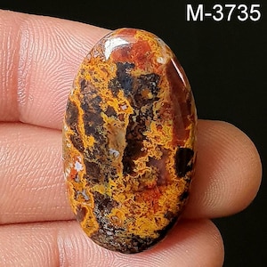 May include: A close-up of a colorful agate cabochon with a mix of red, orange, yellow, and black colors. The stone has a unique, swirling pattern.