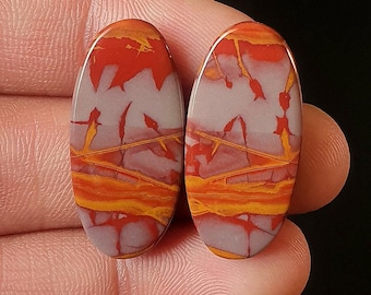 May include: Two oval-shaped cabochons of red, orange, and white jasper with a swirling pattern. The stones are approximately 1 inch long and 1/2 inch wide. M-1946