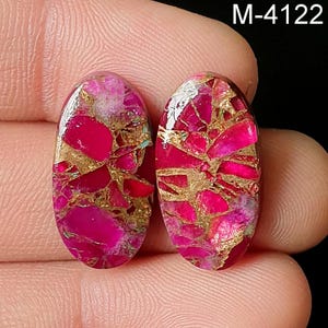 May include: Two oval-shaped gemstones with a vibrant pink and gold mosaic pattern. The gemstones are set against a dark background. The text "M-4122" is in the upper right corner.